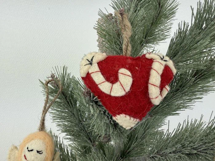 Et filthjerte med candy cane-striber hænger på en fyrretræsgren ved siden af en lille filtengel.