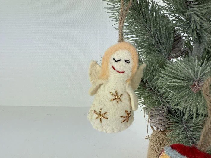 En håndlavet filtengel med guldstjernedekorationer hænger på en grøn juletræsgren.