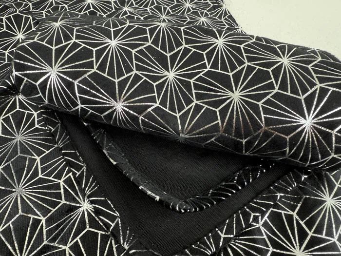 Sort stof med et skinnende, geometrisk sølvstjernemønster, foldet og stablet på en lys overflade.