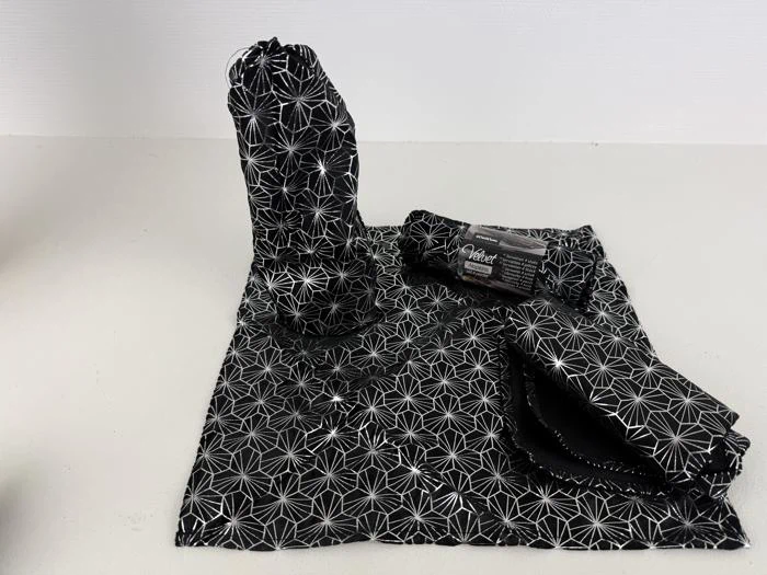 Et sæt sorte stofposer og -klude med et geometrisk hvidt stjernemønster, vist på en lysegrå overflade.