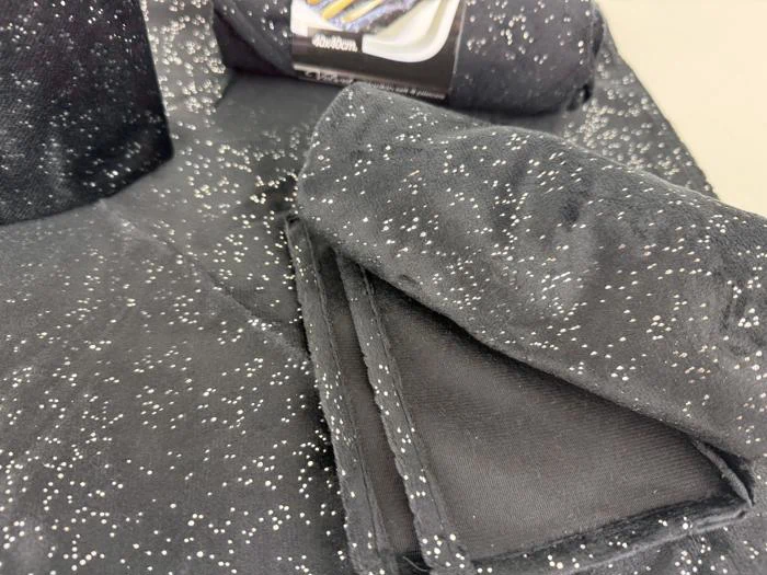 Sort stof med hvide prikker, der ligner stjerner, er foldet og stablet med en etiket, der er delvist synlig i baggrunden.