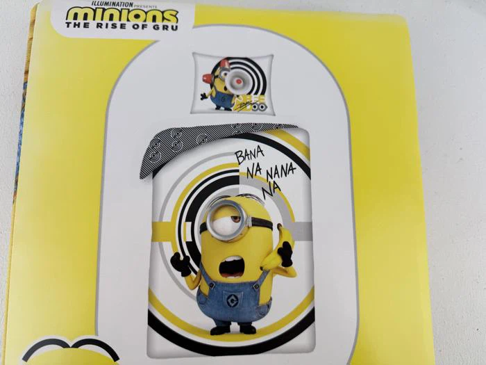 Et sengesæt med Minions-tema med en Minion, der synger med BANA NA NA NANA NA-tekst, gul baggrund og Minions: The Rise of Gru-logoet øverst.