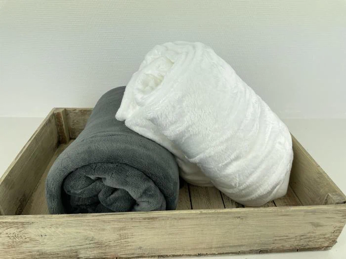 To sammenrullede tæpper, et gråt og et hvidt, placeret side om side i en rustik træbakke mod en lys baggrund.