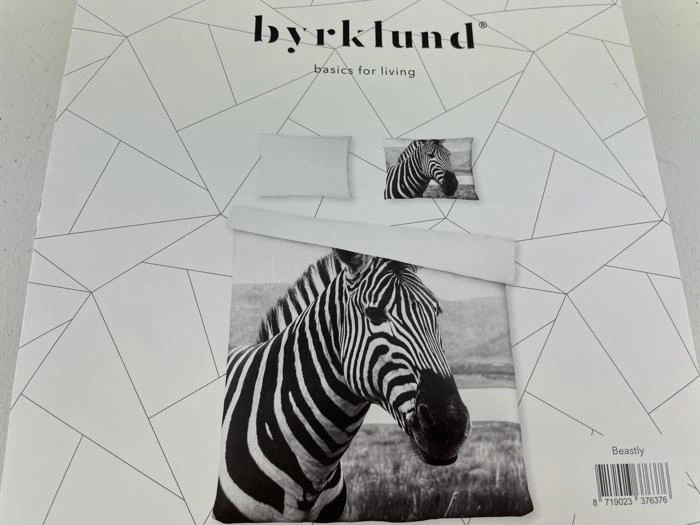 Et sengesæt med sort og hvidt zebraprint vises på emballagen, der er mærket byrklund basics for living med geometriske linjer i baggrunden.