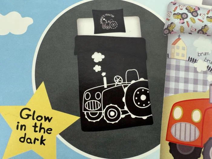 Sort sengetøj med et hvidt, tegneserieagtigt traktordesign, der lyser i mørket, vist med en pude og teksten Glow in the dark i en gul stjerneform.
