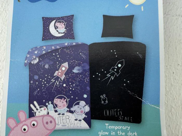 Børnesengetøj med tegneseriedyr i rumdragter, raketter, stjerner og planeter med OUTER SPACE-tekst og selvlysende design i blå, lilla og sorte farver.