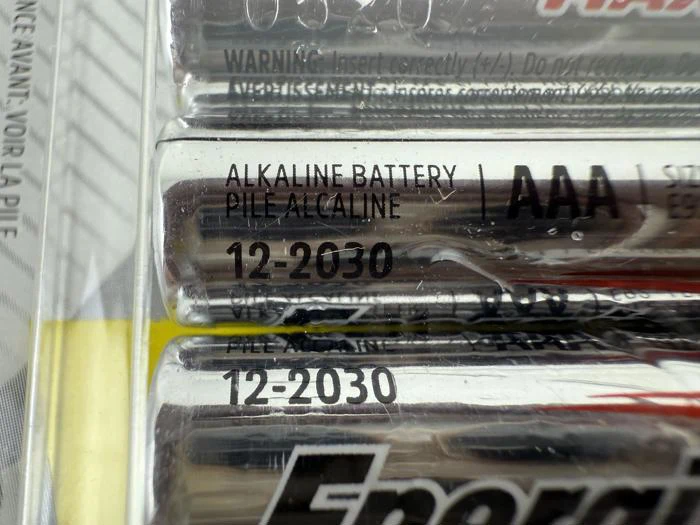 Nærbillede af alkaliske AAA-batterier i emballage, der viser etiketten ALKALINE BATTERY og udløbsdatoen 12-2030, der er trykt på batterierne.