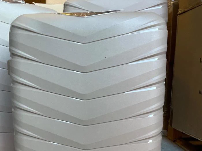 Nærbillede af en stor, lysegrå vandbeholder i plast med vandrette chevronmønstre, placeret indendørs i nærheden af papkasser.