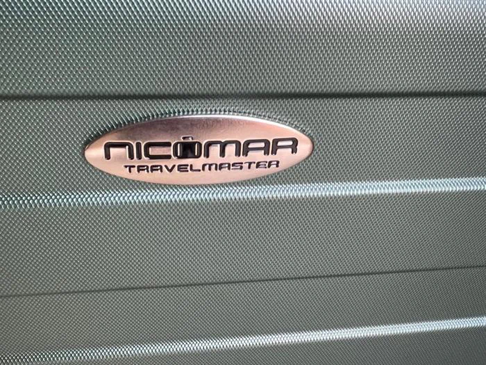 På den ovale metallabel på en grøn kuffert med tekstur står der NICOMAR TRAVELMASTER med fede sorte bogstaver.