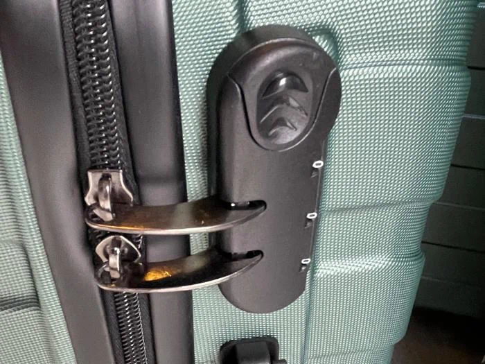 Nærbillede af en grøn struktureret kuffert med en indbygget sort kombinationslås, der holder to lynlåse på plads.