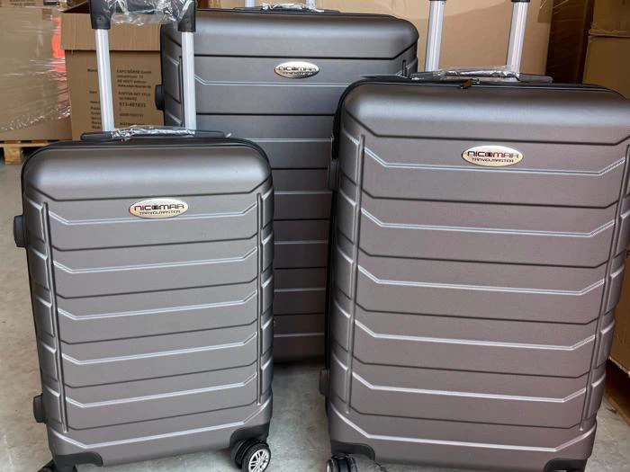 Tre grå kufferter med hård skal i forskellige størrelser står oprejst på et gulv, hver med fire hjul og teleskophåndtag trukket ud.