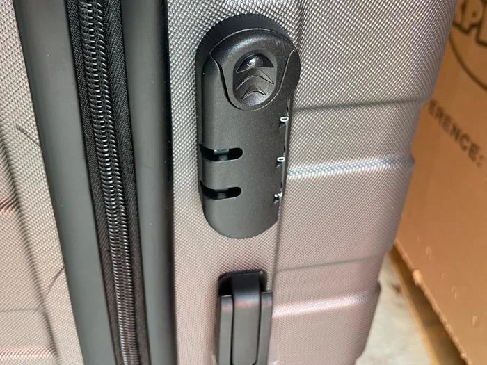 Nærbillede af en grå hardshell-kuffert med indbygget sort kombinationslås og lynlåsdetalje.