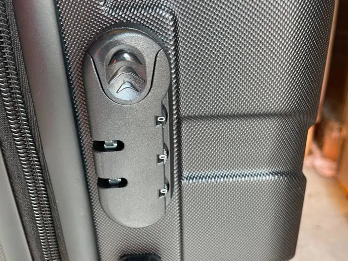 Nærbillede af en sort tekstureret kuffert med en indbygget kombinationslås med tre talskiver og to lynlåstræk, der er sat ind i låsemekanismen.