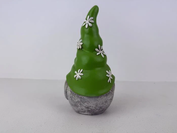 En lille nissefigur med en høj grøn hat dekoreret med hvide blomster og en grå, stenlignende krop er udstillet mod en almindelig hvid baggrund.