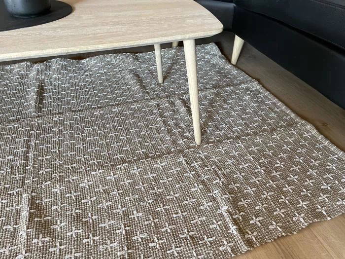 Et beige- og hvidmønstret tæppe ligger på et trægulv ved siden af et lyst træbord og en sort sofa.