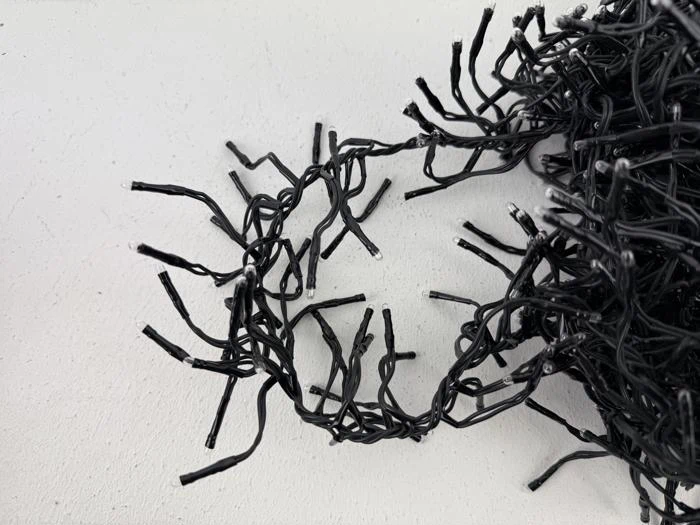 Et nærbillede af en sammenfiltret sort lyskæde på en hvid flade med flere afbrudte ledninger, der stikker ud.