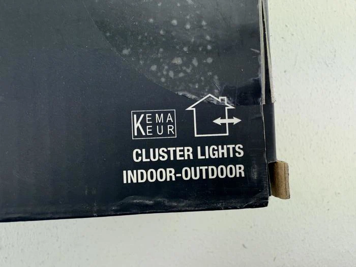 Nærbillede af en sort produktboks med teksten KEMA KEUR Cluster Lights Indoor-Outdoor og et simpelt husomrids-ikon.