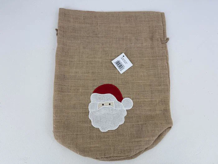 En sæk af jute med en applikation af julemandens ansigt med en rød hue og et hvidt stregkodemærke i toppen.