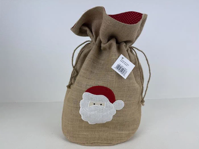 En gavepose af jute med snøre og en applikation af julemandens ansigt og et rødt, prikket for; et stregkodemærke er fastgjort i toppen.