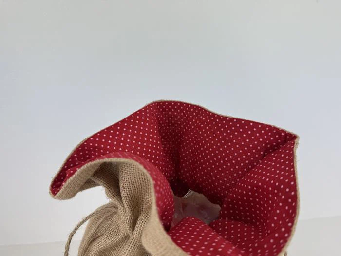 En jutepose med snoretræk og rødt, hvidpudret stoffor, vist delvist åben mod en almindelig hvid baggrund.