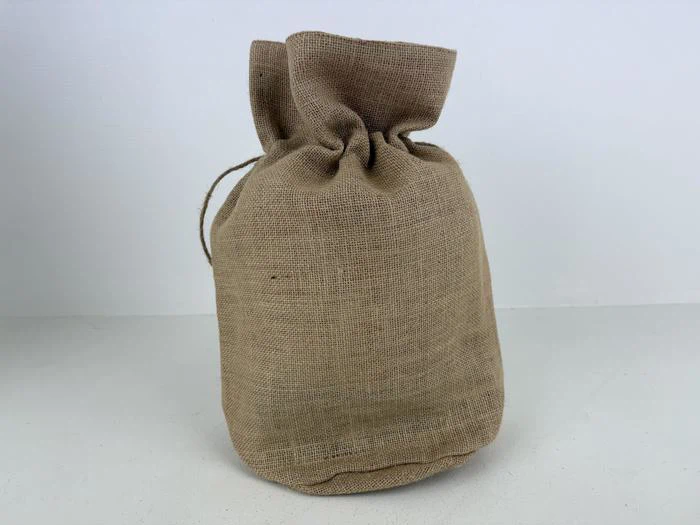 En lille brun jutesæk med snor, der står oprejst på en hvid flade mod en almindelig hvid baggrund.