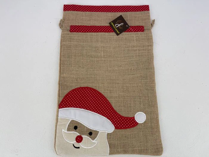 En gavepose af jute med en rød prikket kant og en applikation af julemandens ansigt med en rød hue i nederste venstre hjørne.