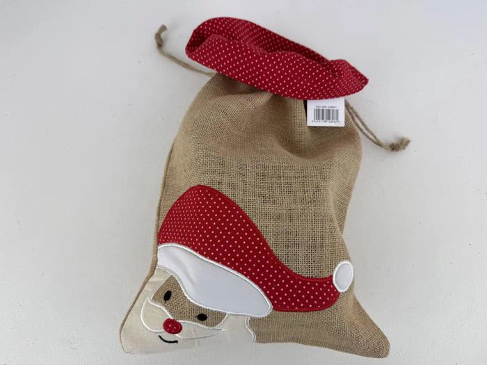 En gavepose af jute med en rød snor og et julemandsansigt med en rød, prikket hue. Et stregkodeklistermærke er fastgjort i toppen af posen.