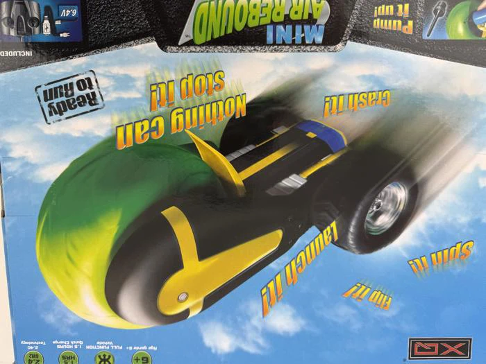 Legetøjsbilens emballage viser et grønt og sort mini air rebound-køretøj med gule detaljer og action-sætninger som Nothing Can Stop It! og Crash It! på en blå baggrund.