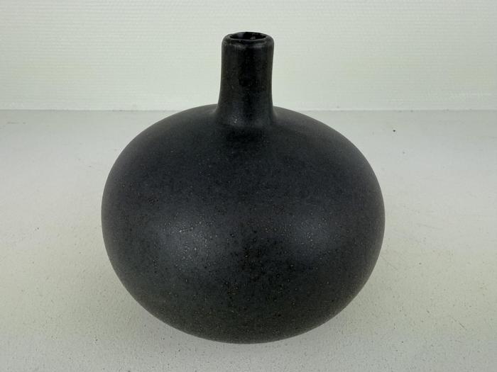 En rund, matsort keramikvase med smal hals og lille åbning, placeret på en lys overflade mod en ensfarvet baggrund.