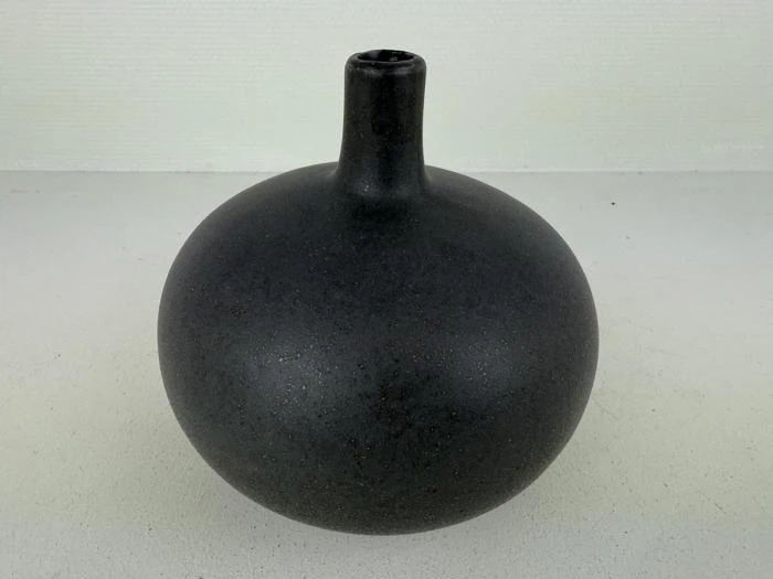 En rund, matsort keramikvase med smal hals og lille åbning, placeret på en lys overflade mod en ensfarvet baggrund.