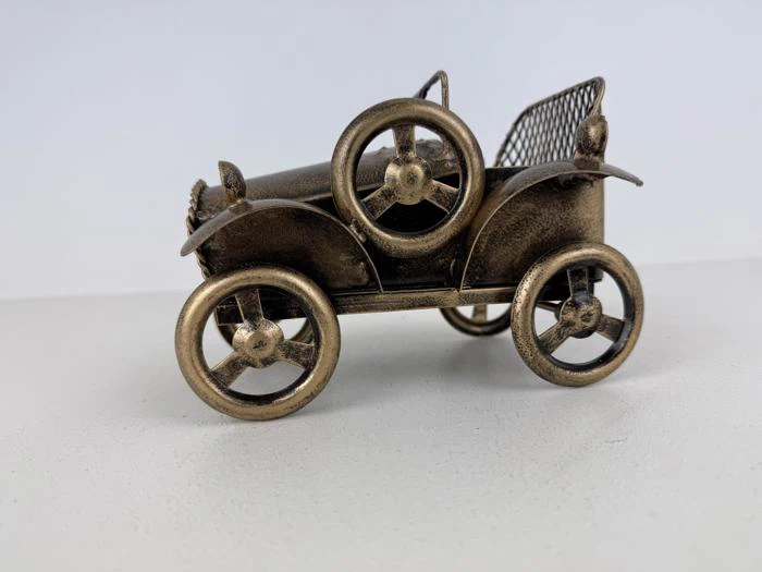 En lille, metallisk model af en gammeldags bil med store hjul, et reservehjul på siden og et netlignende bagsæde.