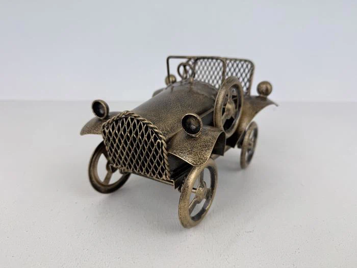 En lille metalmodelbil i vintage-stil med netgitter og egerhjul på en almindelig hvid overflade.