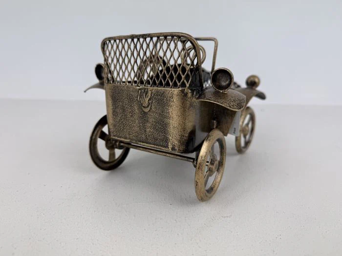 En lille metallegetøjsbil i vintagestil set bagfra med netdetaljer og store egerhjul på en almindelig hvid overflade.