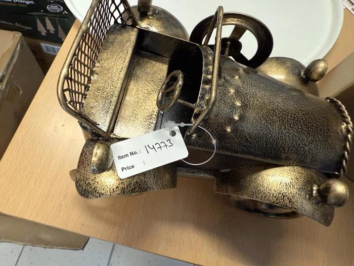 En lille bilfigur i bronze i vintagestil med rat og metalkurv, mærket med varenummer 14973, står på en træplade.