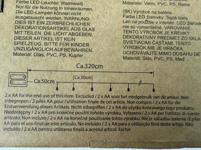 En produktetiket med flersproget tekst om en pyntegenstand, inklusive mål (320 cm længde, 50 cm og 30 cm sektioner) og krav til AA-batterier, vist med et enkelt diagram.