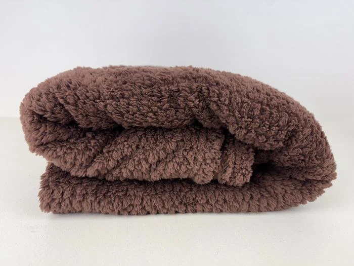 Et blødt, foldet brunt håndklæde hviler på en hvid overflade med en almindelig hvid baggrund.