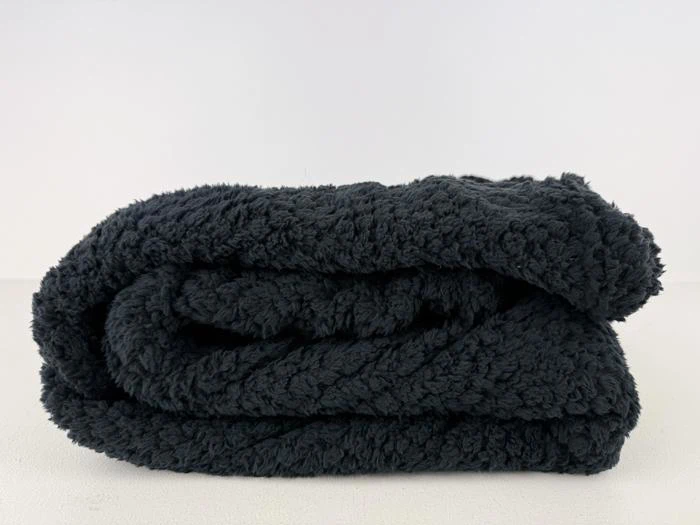 Et sort, fluffy, foldet tæppe ligger på en hvid overflade mod en almindelig hvid baggrund.