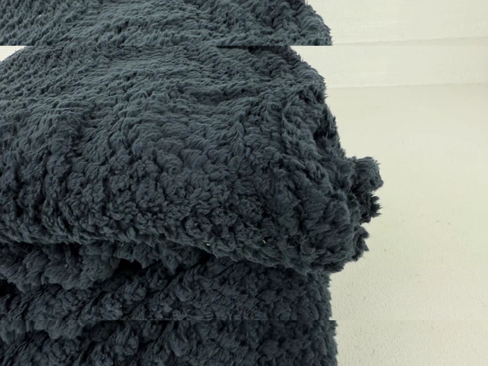 Et nærbillede af et foldet, mørkegråt, luftigt tæppe med en blød, struktureret overflade, placeret på en lys overflade.