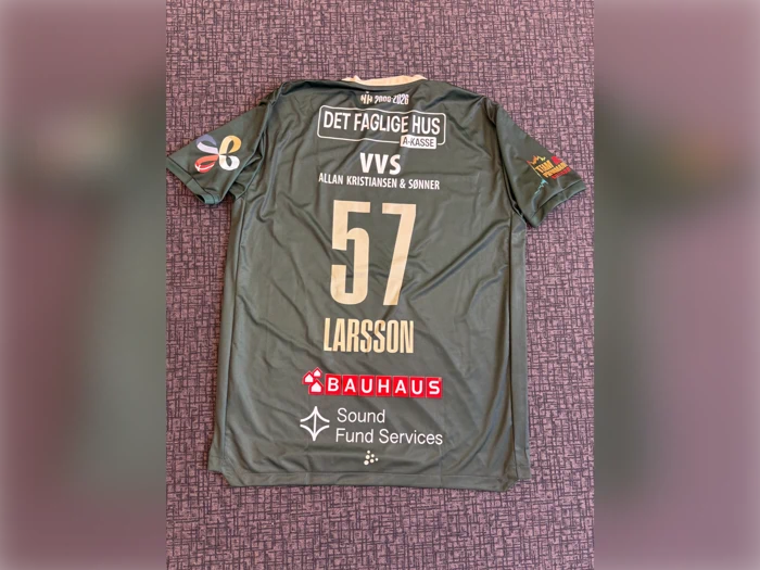 En grøn sportstrøje med nummeret 57 og navnet LARSSON, dækket af adskillige sponsorlogoer, lå fladt på en struktureret overflade.
