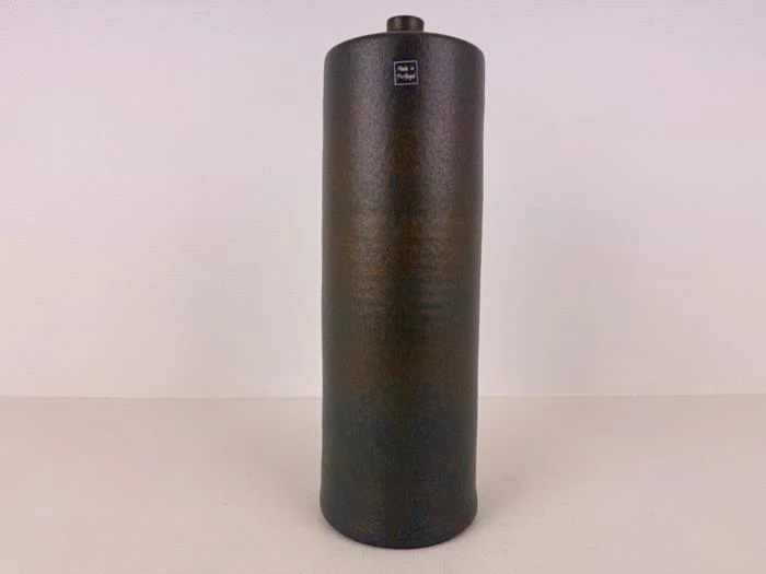 Høj, cylindrisk, mørk keramikvase med en lille rund åbning i toppen og et Made in Portugal-mærke nær kanten, placeret mod en almindelig lys baggrund.