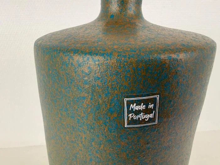En struktureret keramikvase med et blåt og brunt spættet mønster og en etiket med teksten Made in Portugal.