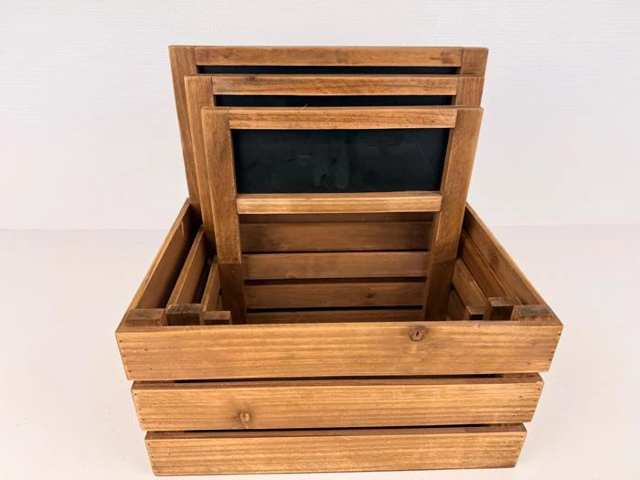 En trækasse indeholder tre små kridttavler med trærammer, der er stablet oprejst inde i den mod en almindelig hvid baggrund.