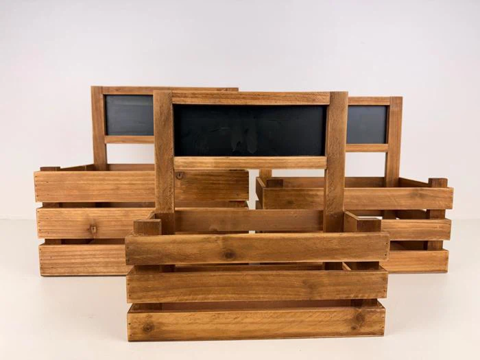 Tre trækasser med håndtag og tomme tavler påsat, anbragt på en hvid flade mod en almindelig baggrund.