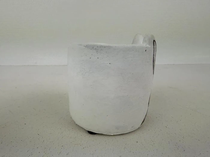 En håndlavet, hvid keramikkop med en ujævn overflade og en diskret hank på en ensfarvet, lys baggrund.