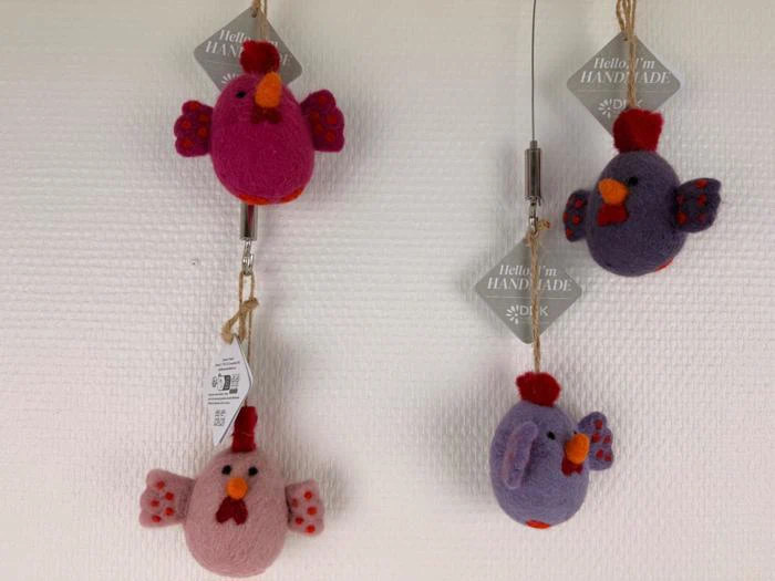 Tre fugleornamenter i filt i pink, rød og lilla med tags, hvor der står Hello, Im HANDMADE, hænger på en struktureret hvid væg.