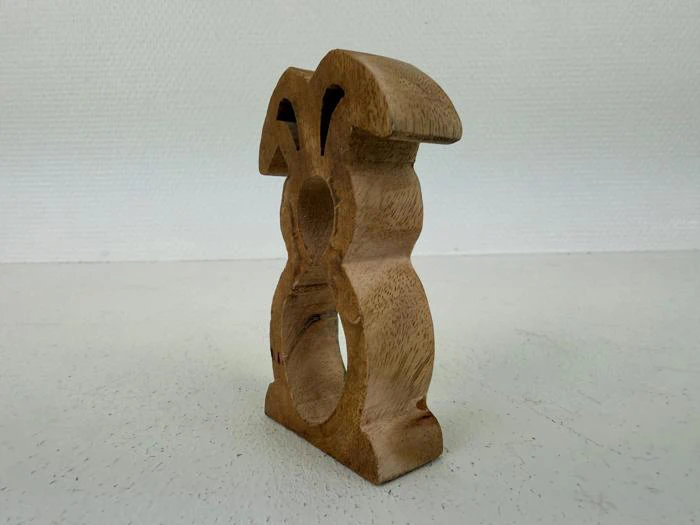 En træskulptur formet som en stiliseret kanin med store ører og en cirkulær udskæring i midten, der står på en hvid flade.