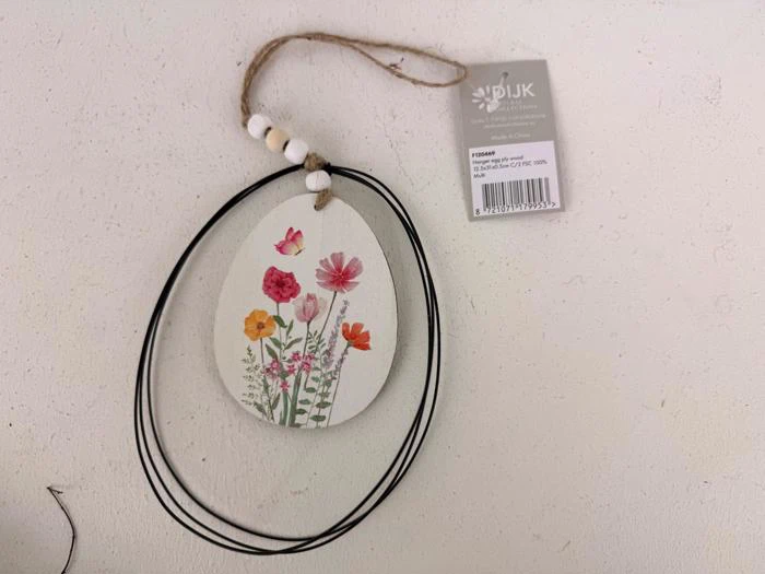 Et ovalt ornament med malede vilde blomster og en jutesnor med træperler, fastgjort til et mærke mærket DIJK.