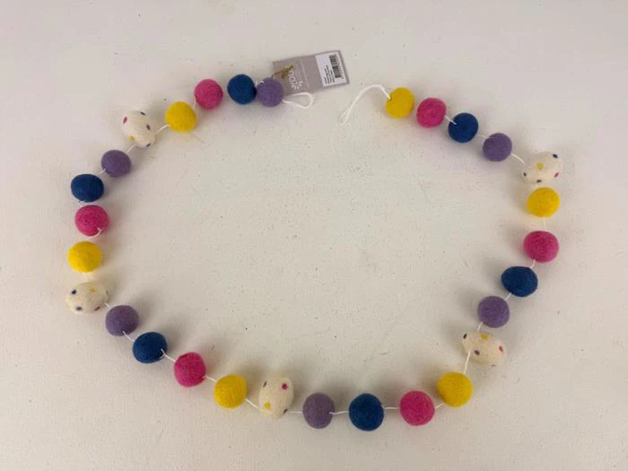 En filtguirlande med farverige kugler i pink, lilla, gul og blå og små hvide filtmus, arrangeret i en løs cirkel på en hvid flade.