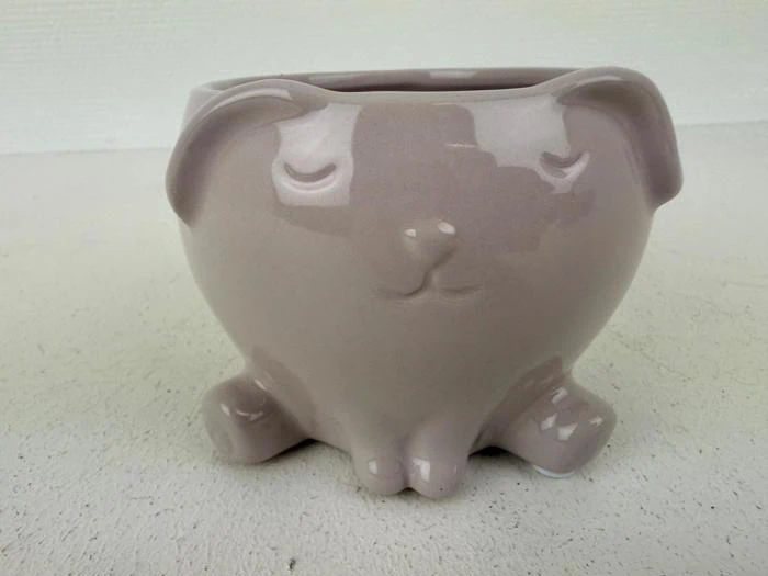 En lysegrå keramisk krukke formet som en siddende hund med lukkede øjne og enkle ansigtstræk.