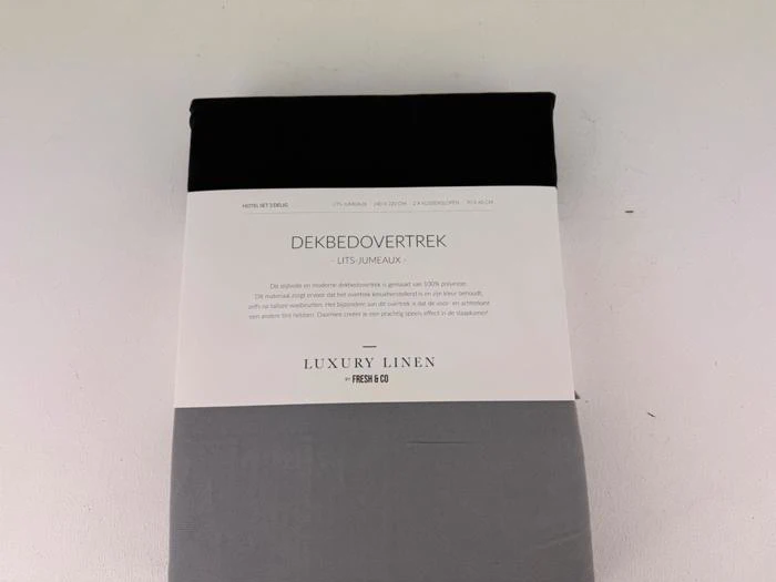 Et pakket luksusdynebetræk i hør i sort og grå, mærket DEKBEDOVERTREK Lits-jumeaux med produktoplysninger på hollandsk på en hvid etiket.
